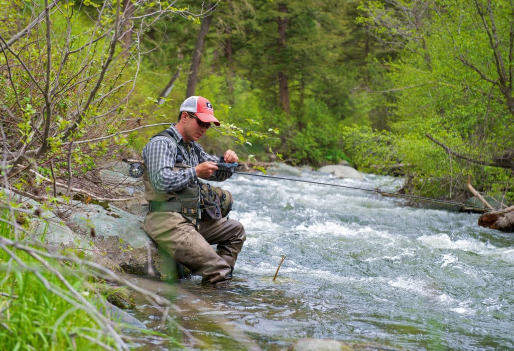 Fisherman working on his reel, sitting on a rock by the river near Mountain Sky's property