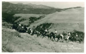 Black and white photo of ranchers riding horses through grassy field at Ox Yoke Ranch