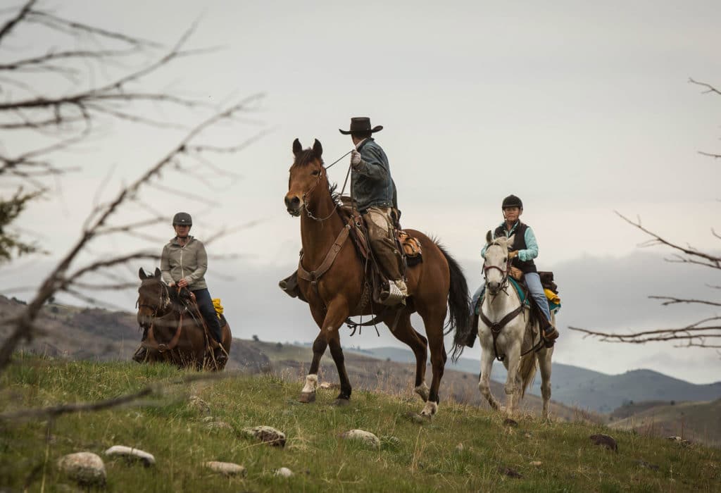 Rancher leading new riders through rocky mountain route on horseback